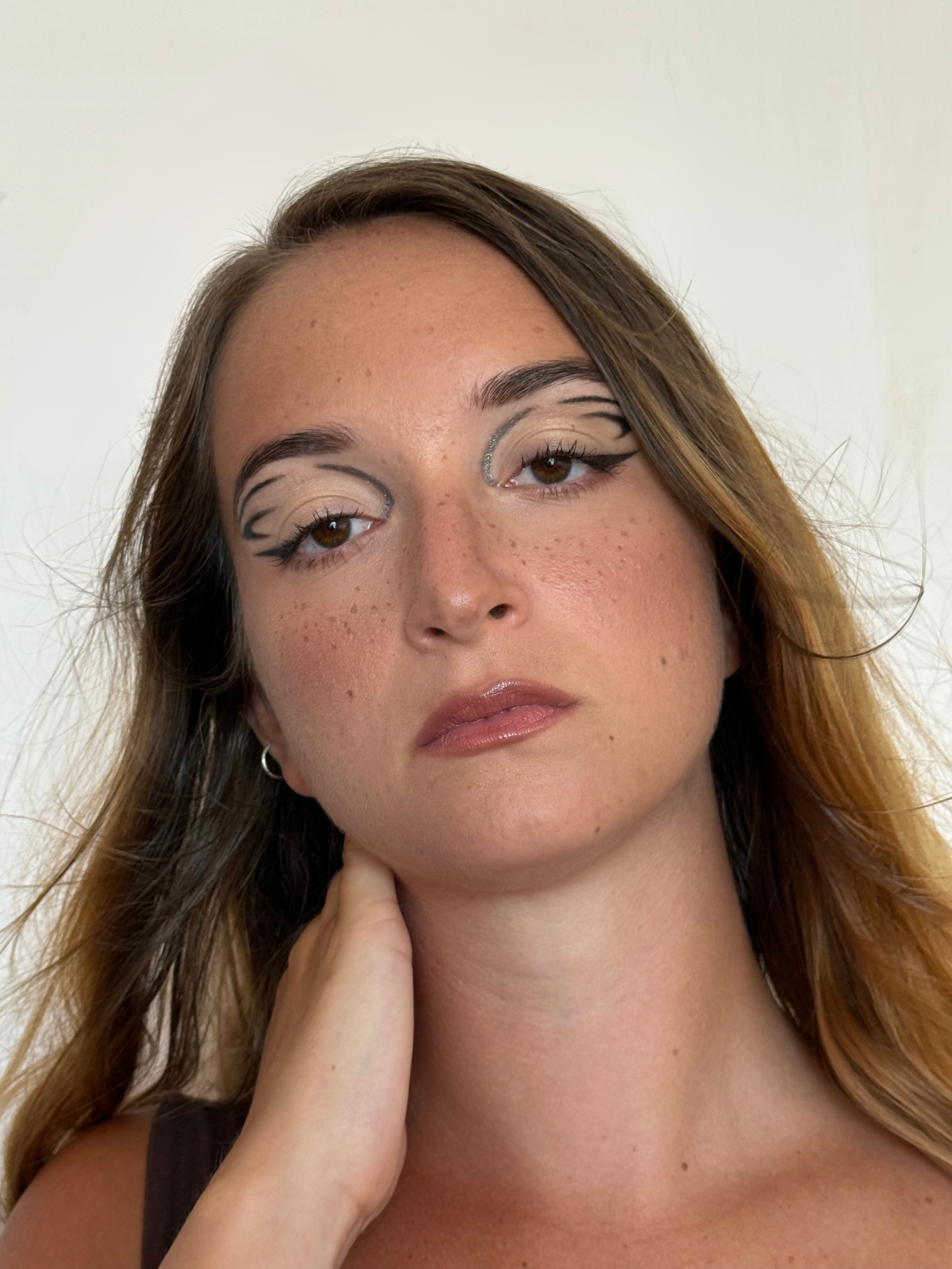 Artistic graphic eyeliner, natural skin, and glossy nude lips.